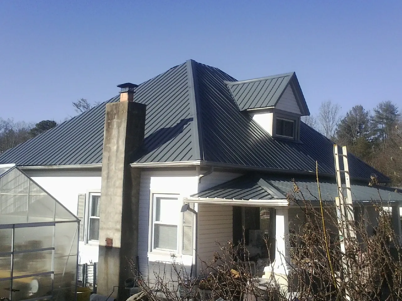 Dark blue standing seam metal roof on a white farmhouse with dormer — Slate & Tile Roof Repair by Roofing Brothers in Port Henry