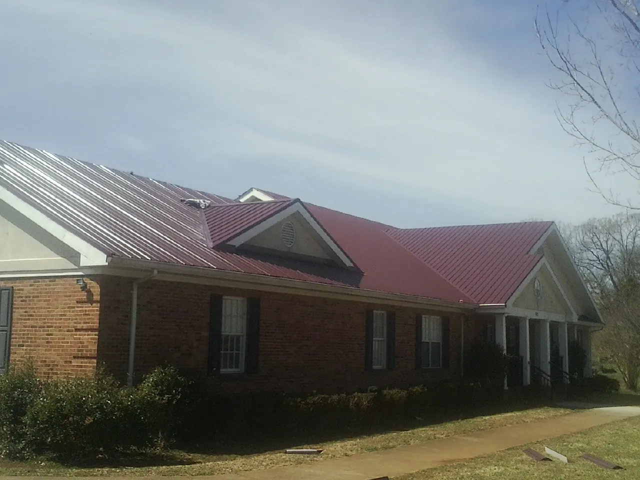 Red metal roof with gabled entries on a long brick building, from a Hail Damage Roof Repair job in Port Henry