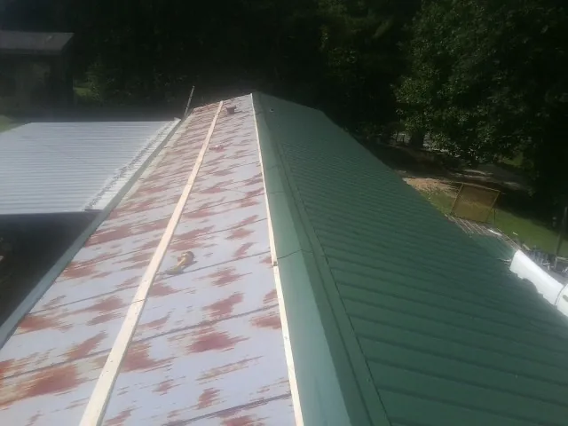 Old rusted panels beside newly installed green metal roofing — Wind Damage Roof Repair by Roofing Brothers in Port Henry
