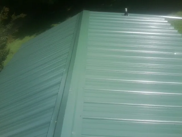 New green metal panels meeting at the ridge of a roof — Flat Roof Repair work by our crew in Port Henry
