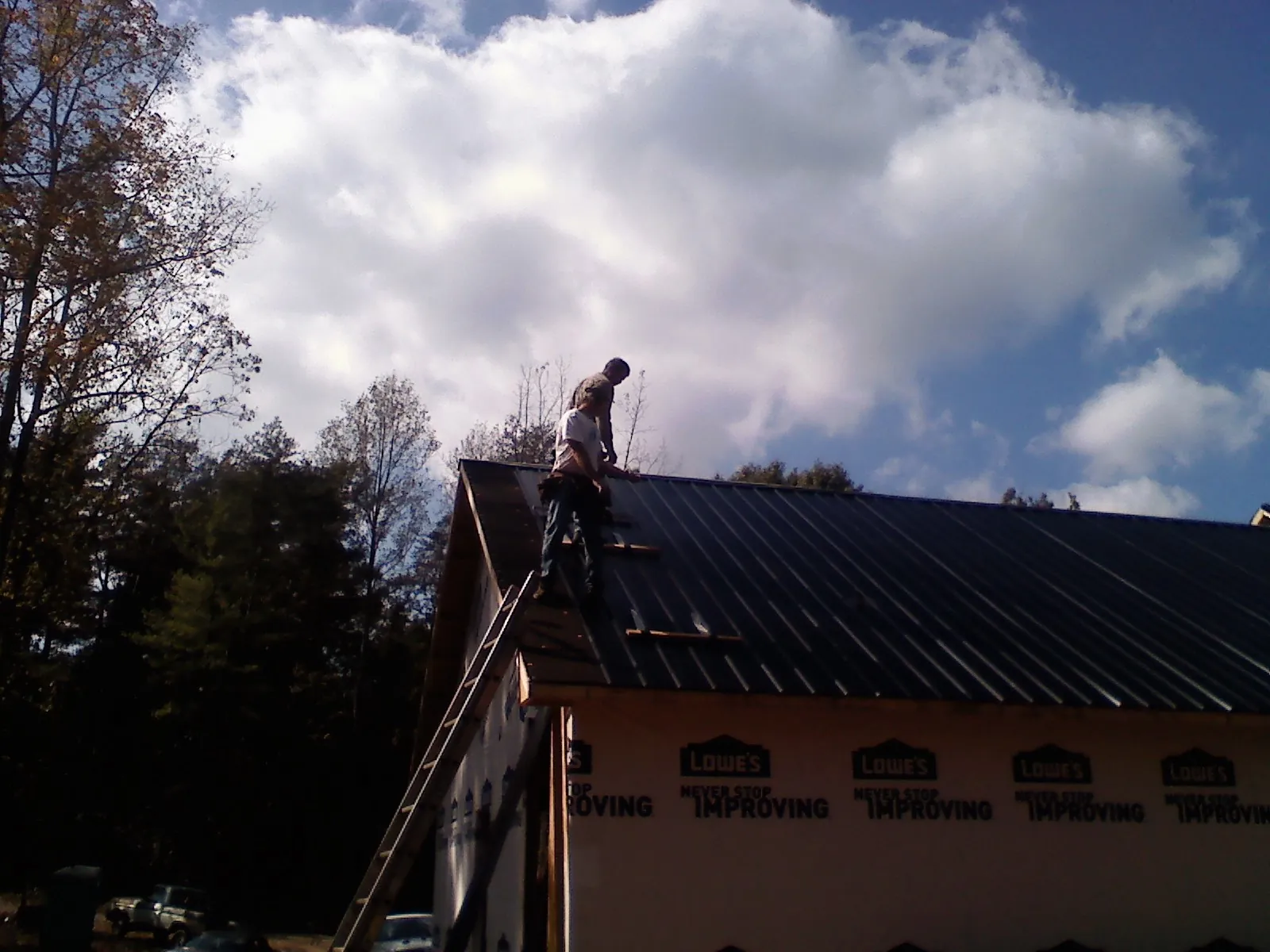 Roofer fastening dark metal panels high against a cloudy sky, from a Roof Inspection job in Port Henry