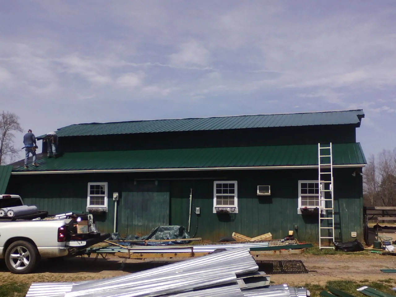 Crew installing green metal roofing on a large green barn in Port Henry