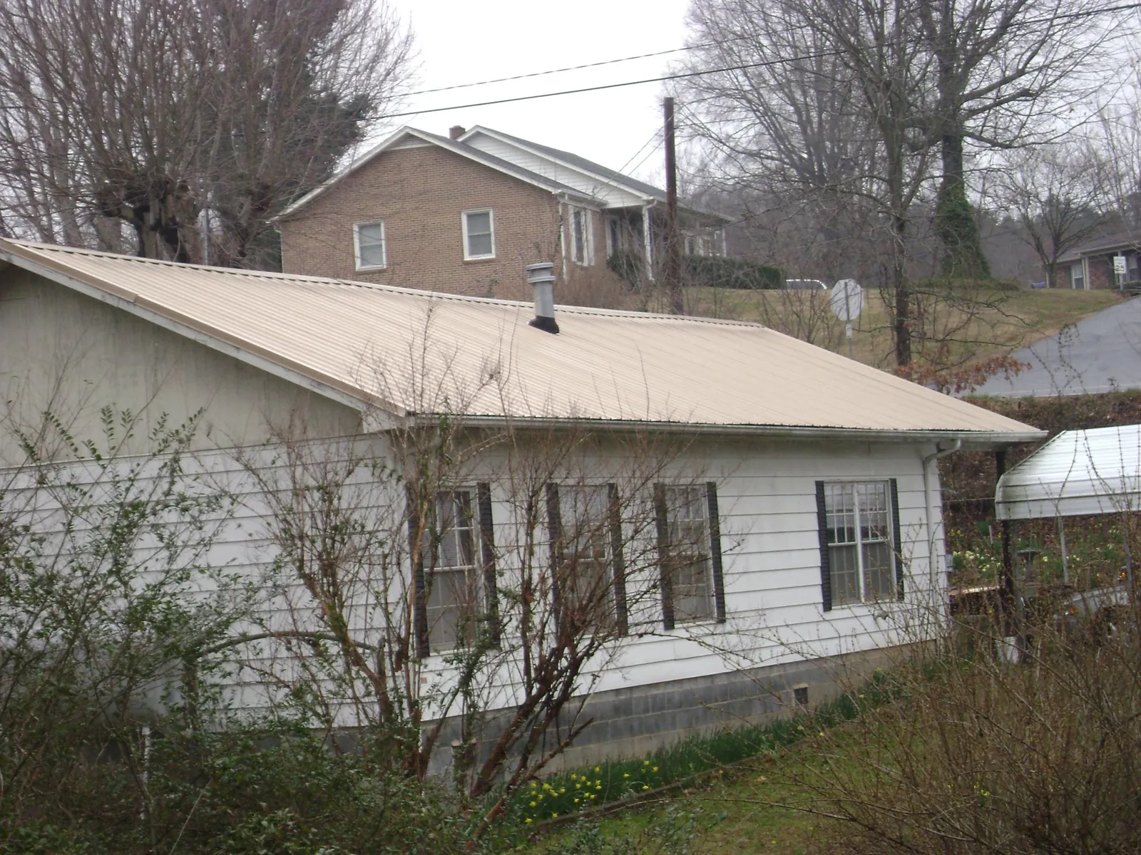 Tan metal roof on a white sided house set into a hillside — Commercial Roofing by Roofing Brothers in Port Henry
