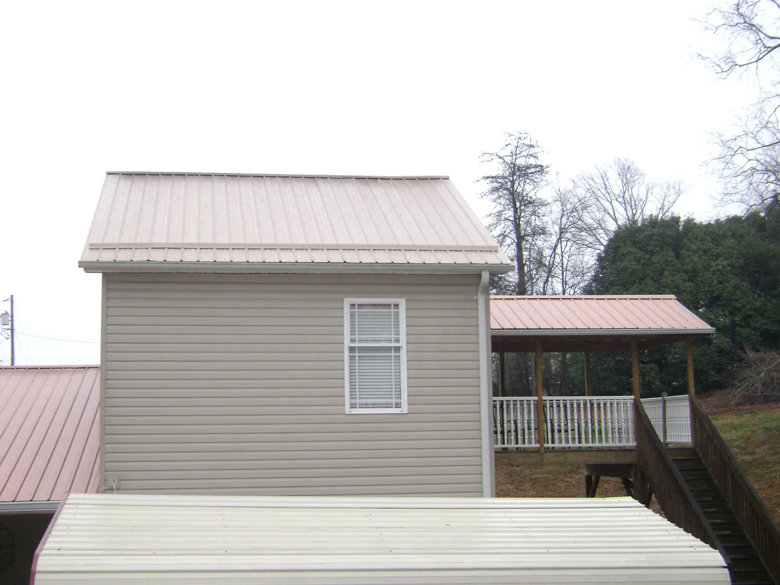 Tan metal roofs on a two story addition and attached porch, from a Roof Replacement job in Port Henry