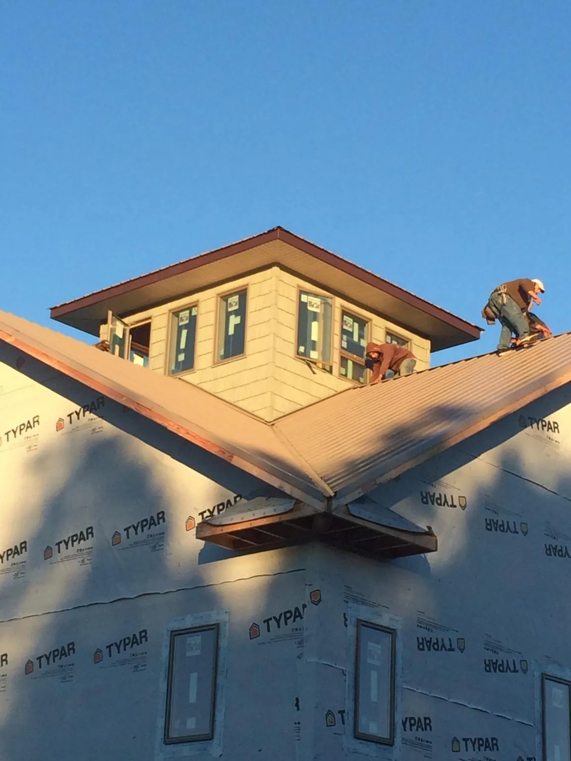 Roofers working around a rooftop cupola on a new metal roof at sunset — Roof Waterproofing in Port Henry by Roofing Brothers